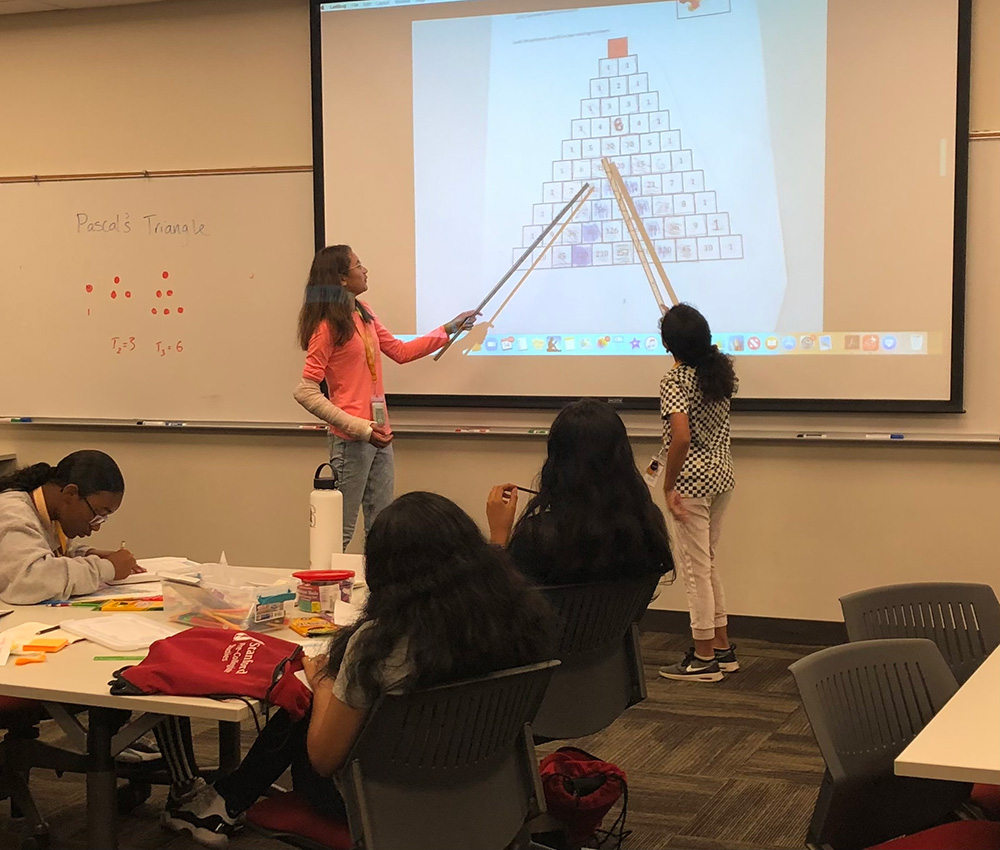 A teacher and student point at a pyramid on an overhead projector